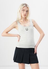 Top gris sin mangas con escote redondeado y bordado de herradura en el centro, combinado con una mini falda negra con pliegues.
