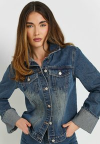 Jeansjacka i varierande nyanser av blått med silverknappar, två bröstfickor och breda, vikta manschetter. Har en lätt urblekt effekt.