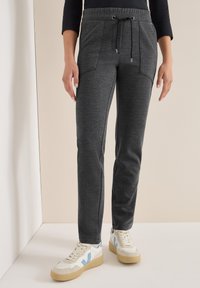 Donkergrijze joggers van een gestructureerde stof, met een tailleband met trekkoord en zijzakken, gecombineerd met lichtgekleurde sneakers.