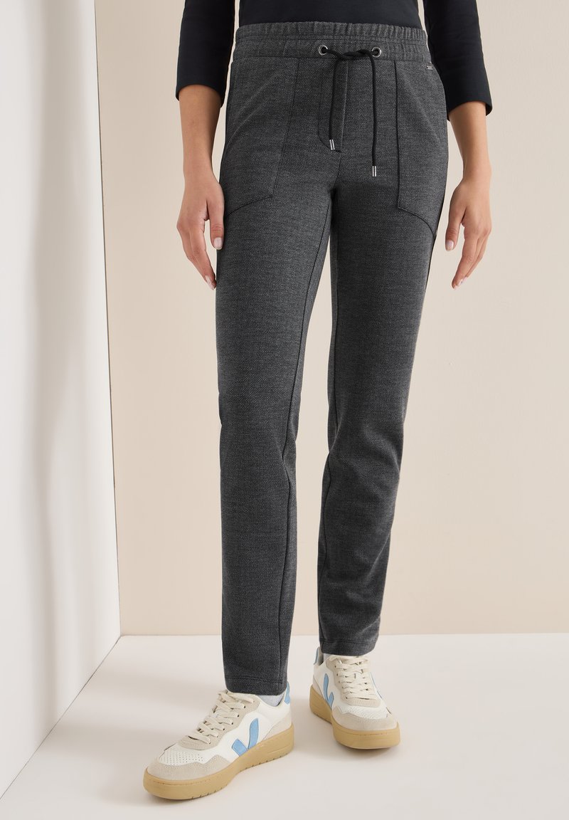 Donkergrijze joggers van een gestructureerde stof, met een tailleband met trekkoord en zijzakken, gecombineerd met lichtgekleurde sneakers.