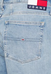 Ljusblå denimjeans bakficka med en liten röd, vit och svart logotyp och en rektangulär etikett ovanför som står "JEANS".