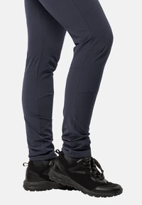 Pantaloni elasticizzati blu navy con cuciture angolari, abbinati a scarpe sportive nere con texture, dotate di lacci e suola robusta.