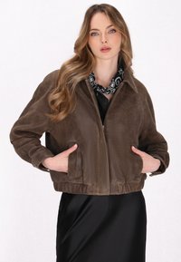 Giubbotto bomber in suede marrone con vestibilità strutturata, tasche laterali, polsini a costine e chiusura con zip, abbinato a una gonna in satin nera.
