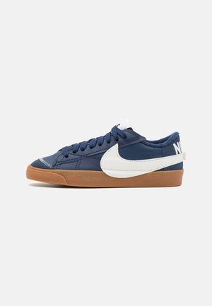 Niedriger dunkelblauer Sneaker mit weißem Nike-Swoosh und Gummisohle, von der Seite auf hellem, einfachem Hintergrund gesehen.
