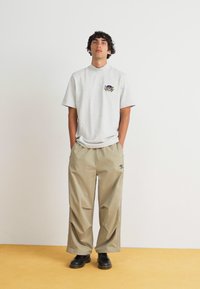 Γκρί κοντομάνικο μπλουζάκι με λογότυπο στο στήθος, συνδυασμένο με χαλαρές μπεζ παντελόνες και μαύρα παπούτσια. Απλός σχεδιασμός και χαλαρή εφαρμογή.