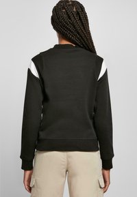 Czarna bluza z białymi akcentami, z prążkowanymi mankietami i dołem. Miękka tekstura, luźny krój i okrągły dekolt. Pokazano widok z tyłu.