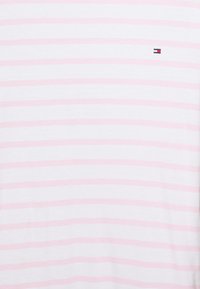 Pruhované tričko s širokými růžovými a bílými pruhy, vyrobené z bavlny, s malým logem na oblasti hrudníku. Měkká textura.