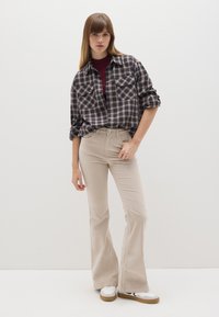 Geruite flanellen shirt in marineblauw en beige, gecombineerd met beige flare-broek en witte sneakers met bruine zolen. Gladde texturen overal.