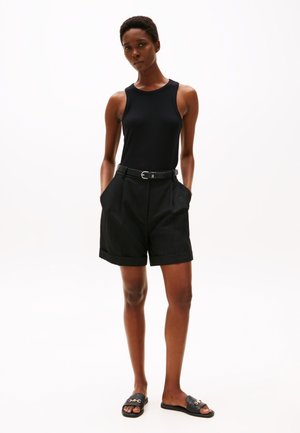 Débardeur noir côtelé associé à un short noir taille haute avec poches et une ceinture. La mannequin porte des sandales noires à glissière avec un accent doré.