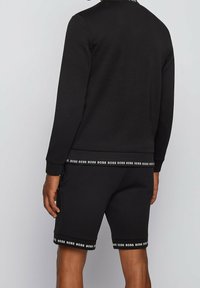 Conjunto de sudadera negra y pantalones cortos fabricado en una mezcla de algodón. Presenta detalles de logo en los puños y la cintura. Textura suave, ajuste relajado.