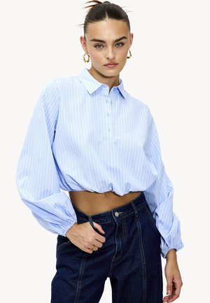 Blouse cropped bleu clair avec des rayures blanches verticales, col boutonné et manches bouffantes, associé à un jean en denim foncé taille haute.