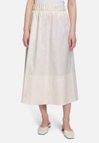 Kremowa spódnica o średniej długości z elastycznym pasem, gładką fakturą i nieco ciemniejszym dołem. Noszona z kremowymi butami na słupku.