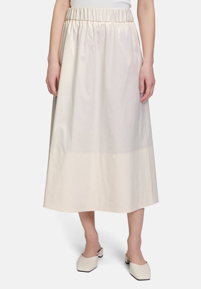 Kremowa spódnica o średniej długości z elastycznym pasem, gładką fakturą i nieco ciemniejszym dołem. Noszona z kremowymi butami na słupku.