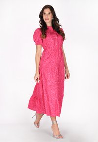 Rochie maxi cu imprimeu de leopard roz, cu mâneci scurte tip puff, guler înalt și talie strânsă. Sandalele argintii cu curele completează ținuta.