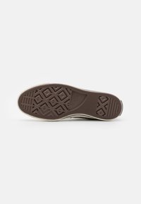 Suela de zapato de goma marrón con un patrón texturizado que presenta formas geométricas y un borde lateral blanco. Diseño plano y durable, adecuado para uso casual.