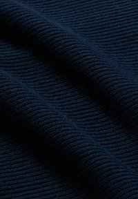 Tmavě modrá pletená látka s viditelnou jemně žebrovanou strukturou, složená tak, aby vytvářela měkké stíny a odlesky.