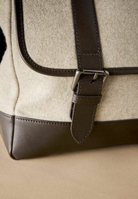 Beige felt bag with dark brown leather accents. Features a prominent buckle on the strap and contrasting stitching along the edges.