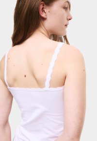 Biały top na cienkich ramiączkach z koronkową lamówką, o prostym kroju i dopasowanym fasonie. Tkanina wydaje się gładka, z minimalnymi detalami tekstury.