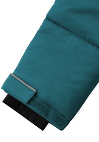 Türkisfarbenes Ärmelteil aus strukturiertem Stoff mit grauem Akzent und schwarzem Klettverschluss am Bündchen. Glatte Oberfläche mit leichter Polsterung.