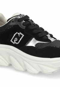 Baskets en daim noir avec accents argentés, lacets ronds et semelle épaisse blanche présentant un motif texturé ainsi qu'un logo métallique décoratif.