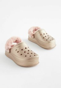 Guld-farvede klipklappere med en skinnende finish, udstyret med en lyserød faux fur-foring, cirkulære perforeringer og en forhøjet platformsål.