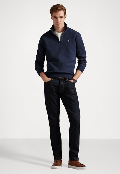 Marineblå zip-up sweatshirt med ribbede manchetter, parret med mørke denimjeans. Brune sneakers har en struktureret overdel med en hvid sål. Klassisk pasform.
