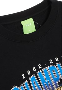 Sudadera negra con cuello redondo, que presenta un diseño gráfico colorido que incluye texto blanco y azul. Etiqueta verde interior con "HUF" y talla "M."