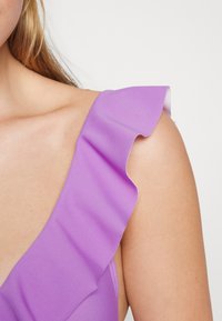 Vestido lilás com alça de ombro com babados e tecido suave e brilhante. A vista em close destaca a textura e o caimento suave.