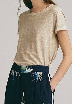 T-shirt beige a maniche corte con scollo rotondo classico, realizzato in tessuto morbido, abbinato a pantaloni navy con motivi floreali e una vita vivace.