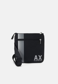 Borsa a tracolla nera con superficie texturizzata, striscia argentata e logo frontale "AX MILANO/NEW YORK." Dotata di tracolla regolabile e chiusura con zip.