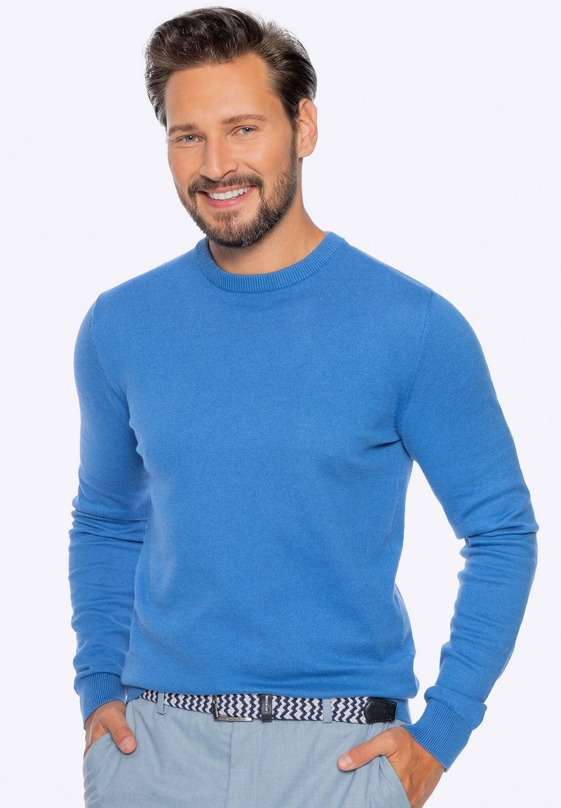 Blauer Rundhalsausschnitt-Pullover mit langen Ärmeln, aus einem weichen Strickmaterial. Verfügt über einen gerippten Kragen und Bündchen, getragen über hellen Hosen.