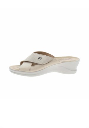 Sandalia de mujer de color beige claro con puntera abierta, tacón cuña bajo, tira ajustable con detalle floral en relieve y pequeño emblema decorativo plateado.
