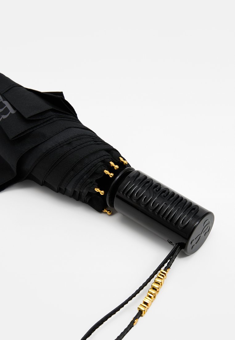 Schwarzer, geschlossener Moschino-Regenschirm mit goldenen Spitzen an den Streben, einem schwarzen Griff mit eingeprägtem Markennamen und einem Handgelenkband mit goldenen Perlen.