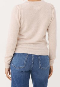 Sweter z jasnobeżowego dzianego materiału z bufkami na ramionach i okrągłym dekoltem, zestawiony ze średnioniebieskimi, wysokim stanem jeansami z klasycznymi tylnymi kieszeniami.