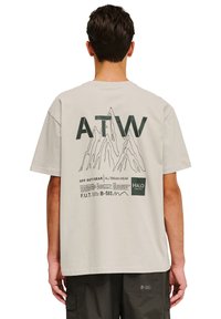Lys beige bomulds t-shirt med et bjerggrafik, "ATW" tekst og sorte trykdetailler på ryggen. Korte ærmer, løs pasform.