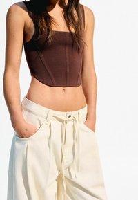 Brown cropped top with a square neckline and ribbed texture, paired with high-waisted cream trousers featuring side pockets and a tie front.