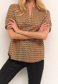 Haut à manches courtes avec un motif géométrique aux tons terreux orange et vert, doté d'un col en encoche et d'une coupe décontractée.