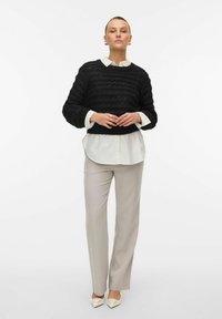 Svart texturerad tröja med vågmönster, över en vit skjorta med krage, matchat med ljusgrå byxor och vita klackar med spetsig tå.