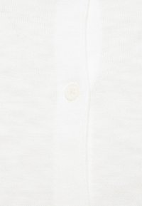 Cardigan bianco a maglia con una consistenza morbida, caratterizzato da un singolo bottone di chiusura davanti. Design semplice, materiale leggero.