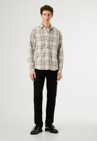 Karierte Button-Down-Bluse in Beige und Oliv, aus weichem Stoff, kombiniert mit schwarzen Hosen und schwarzen Schnürschuhen.