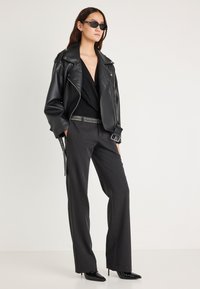 Μαύρο δερμάτινο biker μπουφάν, μαύρο τοπ, γκρι φαρδιά παντελόνια, ζώνη με διακοσμητικά στοιχεία, μαύρα μποτάκια με ψηλό τακούνι και μαύρα γυαλιά ηλίου.
