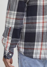 Camisa a cuadros con patrones en azul marino, rojo y blanco. Puños abotonados, tejido ligero y dobladillo sin meter. Mezcla de algodón con textura suave.