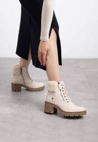 Botas de tobillo beige con un puño forrado de piel, cordones en la parte delantera, cremallera lateral y suela texturizada. Fabricadas con material suave y con un tacón grueso.