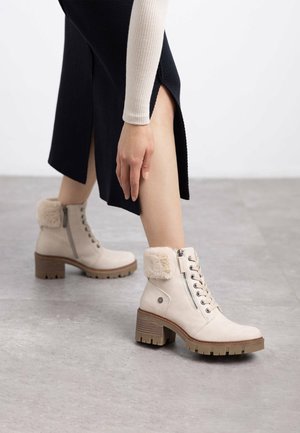 Botas de tobillo beige con un puño forrado de piel, cordones en la parte delantera, cremallera lateral y suela texturizada. Fabricadas con material suave y con un tacón grueso.