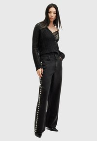 Svart virkad kofta över en svart spets-topp, parat med vida svarta jeans med metalliska nitar längs sömmarna. Spetsiga svarta skor.