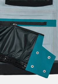 Schwarzes und graues Innenfutter der Tasche mit einer türkisfarbenen Reißverschlusstasche, glänzenden Druckknöpfen, glattem Stoff und einem markierten elastischen Band am Rand.