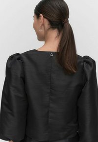 Sort cropped top med pufærmer, en glat tekstur og en cirkulær metalaccent bagpå. Simpelt og skræddersyet design.