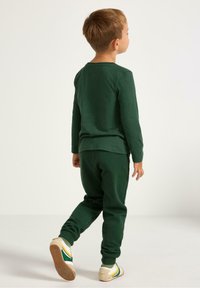 Camicia verde di cotone a maniche lunghe e pantaloni abbinati. Tessuto morbido con una vestibilità rilassata. Sneakers con dettagli gialli, verdi e bianchi.