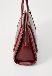 Borsa a mano in pelle rossa con chiusura a zip, caratterizzata da un motivo trapuntato e una forma triangolare strutturata. Texture liscia con doppio manico.