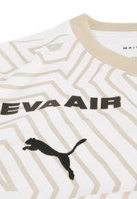 Hvid sportstrøje med beigefarvet zigzag-mønster, sort "EVA AIR" tekst og sort Puma-logo. Har en beigefarvet ribbet krave og struktureret stof.